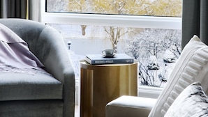 A modern living room with a large window, a sofa, a side table, and a small table with a book and a cup.