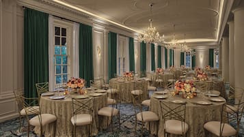 Un comedor formal con mesas redondas, sillas doradas y cortinas verdes.