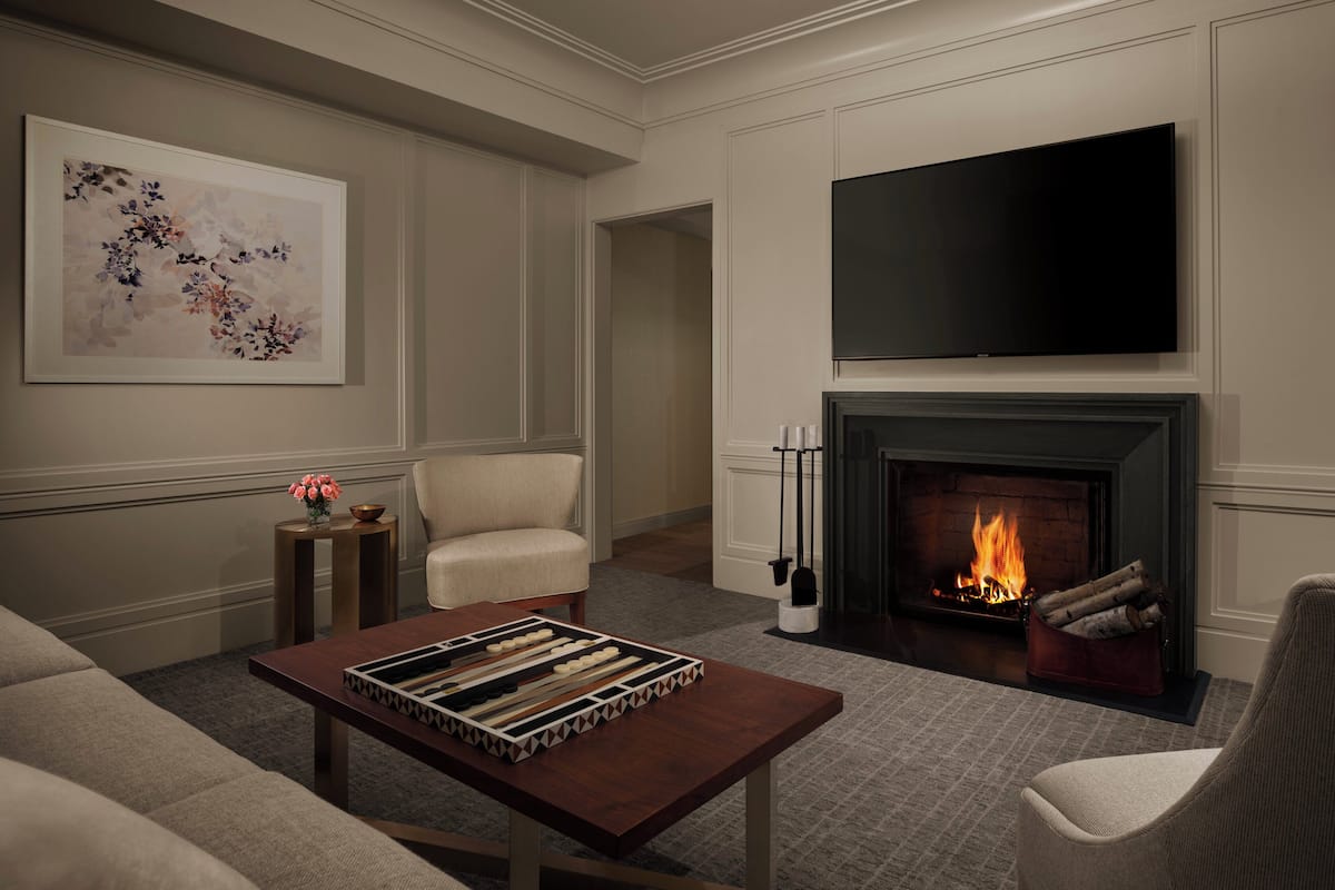 A living room with a fireplace, a flat-screen TV, a chessboard, and a framed floral artwork on the wall.