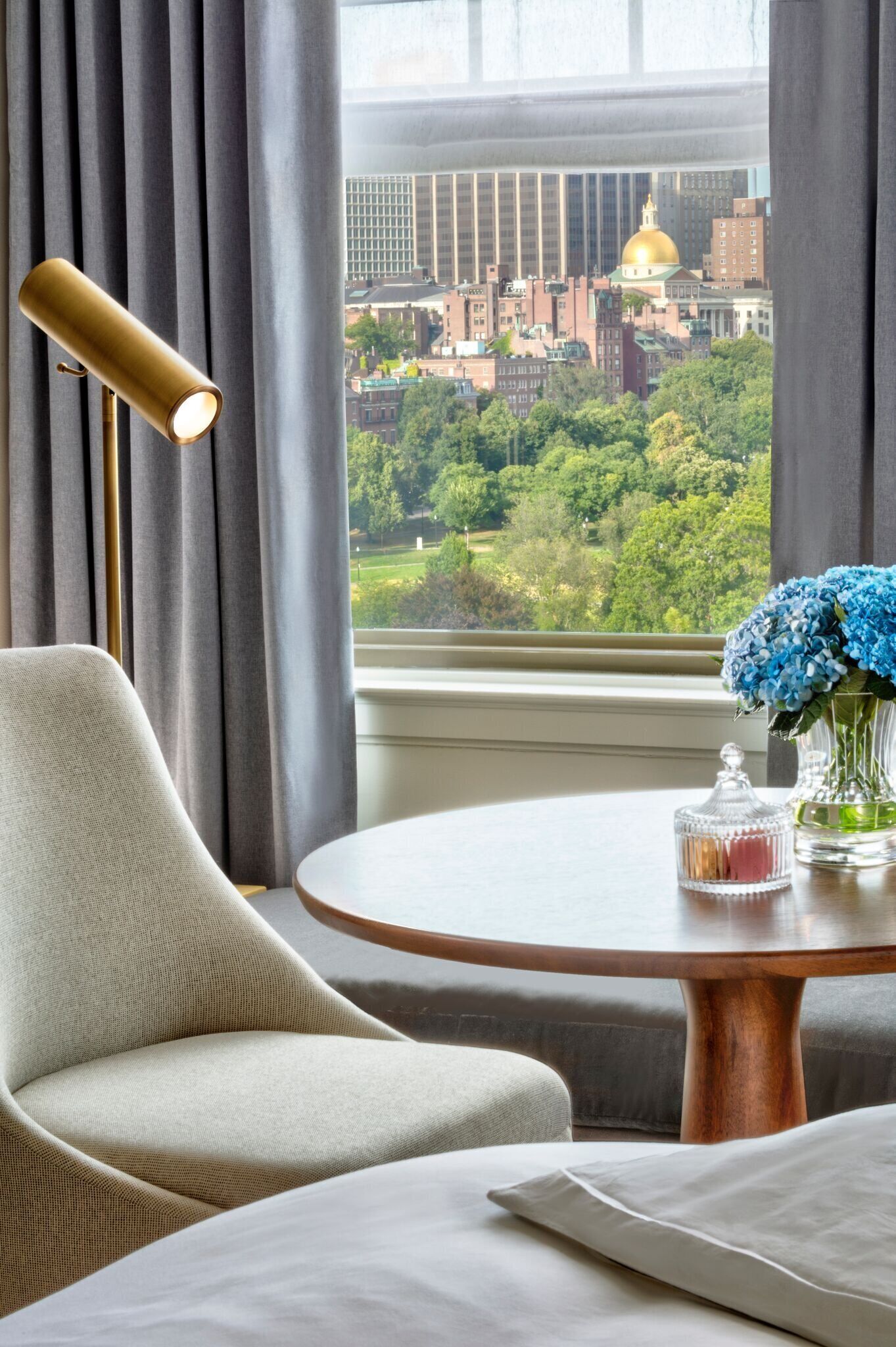 Ein Hotelzimmer mit Blick auf die Stadt, ein runder Holztisch mit Blumenvase und ein moderner Sessel.