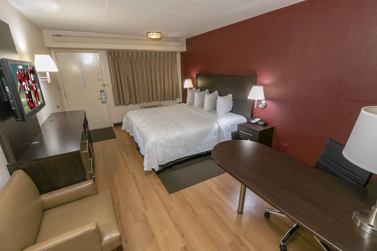 Ein Hotelzimmer mit einem Bett, einem Schreibtisch, einem Stuhl, einem Fernseher und einer Lampe.