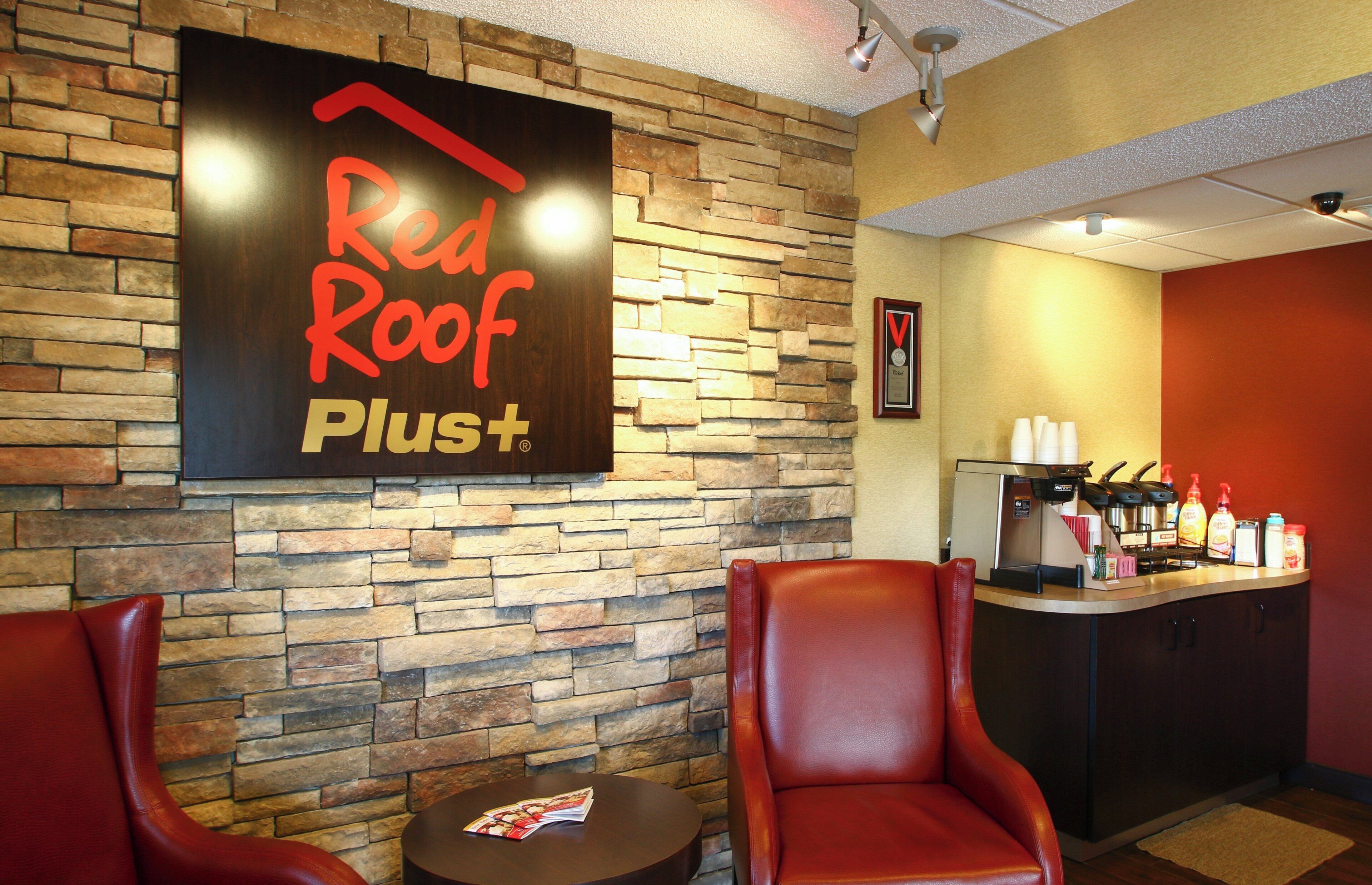 Intérieur d’un café Red Roof Plus+ avec des murs en pierre, des fauteuils en cuir, une machine à café et un menu posé sur une table.