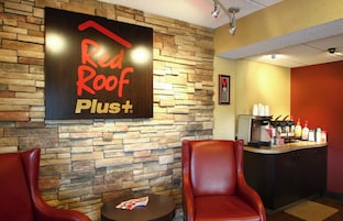 Interior de una cafetería Red Roof Plus+ con paredes de piedra, sillas de cuero, una máquina de café y un menú sobre una mesa.