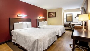 Une chambre d’hôtel avec deux lits, un bureau, une chaise, un miroir et un tableau au mur.