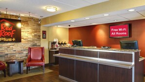 Un hall d'accueil d'hôtel avec un mur en pierre, une enseigne « Red Roof Plus », une affiche indiquant que le Wi-Fi est gratuit, un comptoir d'accueil et un fauteuil en cuir rouge.