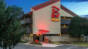 Un hôtel reconnaissable à son grand panneau rouge sur le toit, à sa façade en pierre et à son parking situé devant l’entrée.
