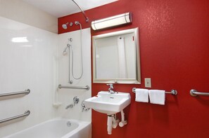 A bathroom with a white bathtub, a sink with a mirror above it, and a shower with a handheld showerhead.