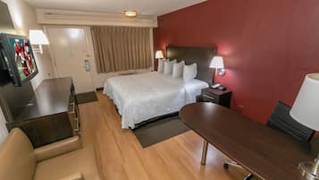 A hotel room with a bed, bedside tables, a desk, a chair, and a television.