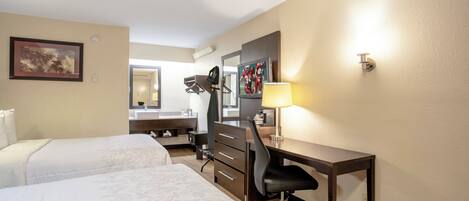 A hotel room with two beds, a desk, a chair, a mirror, a television, and a lamp.