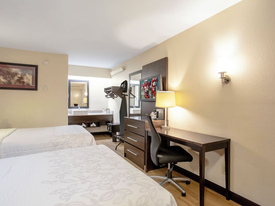 Une chambre d’hôtel avec deux lits, un bureau, une chaise, un miroir, une télévision et une lampe.