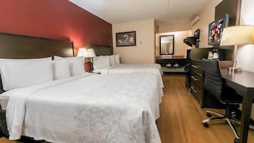 Une chambre d’hôtel avec un lit double, un bureau, une chaise, une télévision et une salle de bain équipée d’un miroir et d’un lavabo.