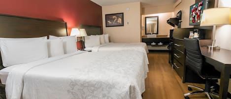A hotel room with a double bed, a desk, a chair, a TV, and a bathroom with a mirror and sink.