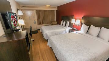 A hotel room with two beds, a desk, a television, and a minibar.
