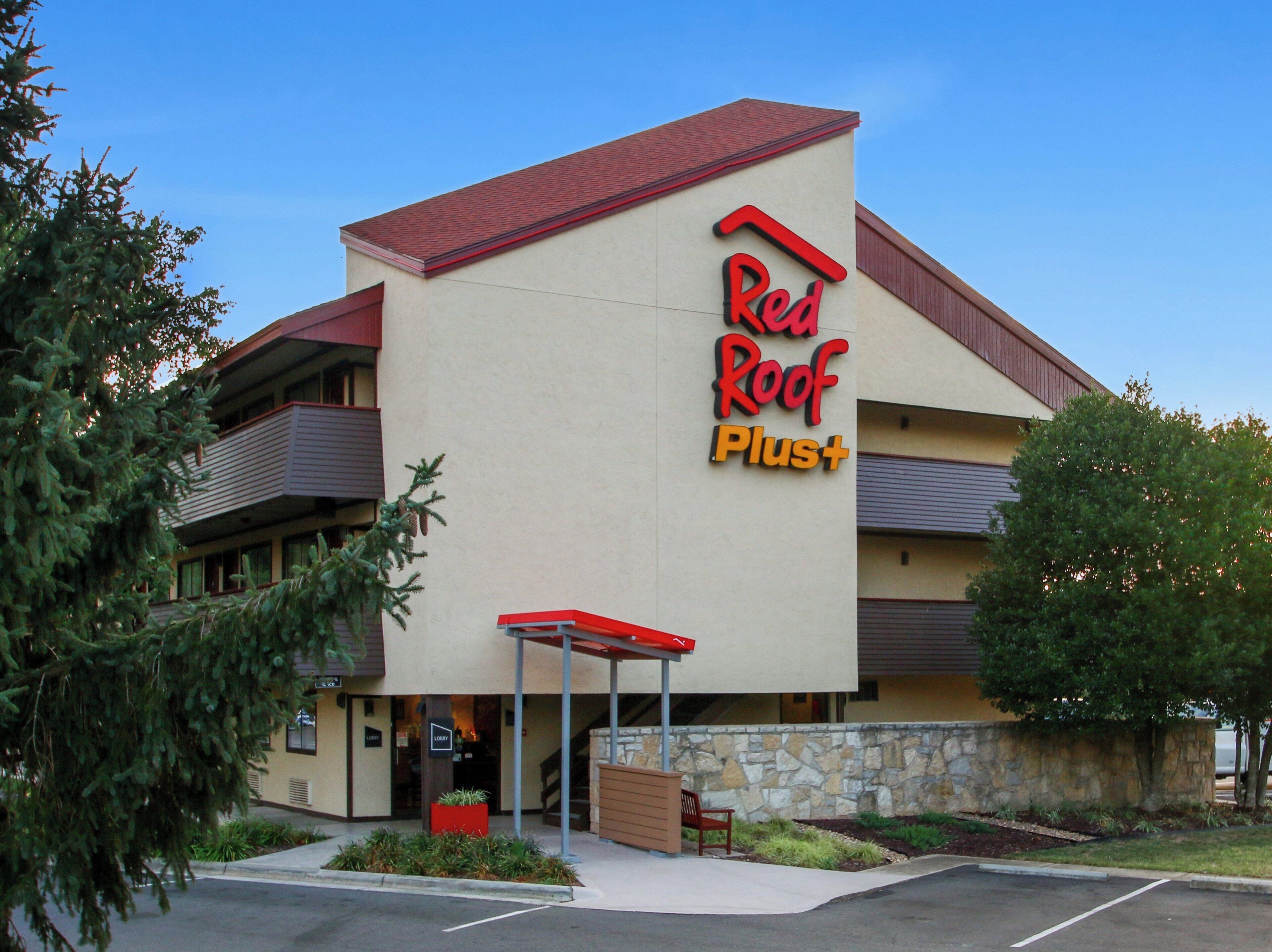 Un hotel Red Roof Plus con techo rojo, fachada de piedra y entrada cubierta.