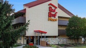 Un hôtel Red Roof Plus doté d’un toit rouge, d’une façade en pierre et d’une entrée abritée.