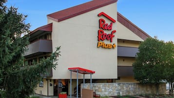 Un hotel Red Roof Plus con techo rojo, fachada de piedra y entrada cubierta.