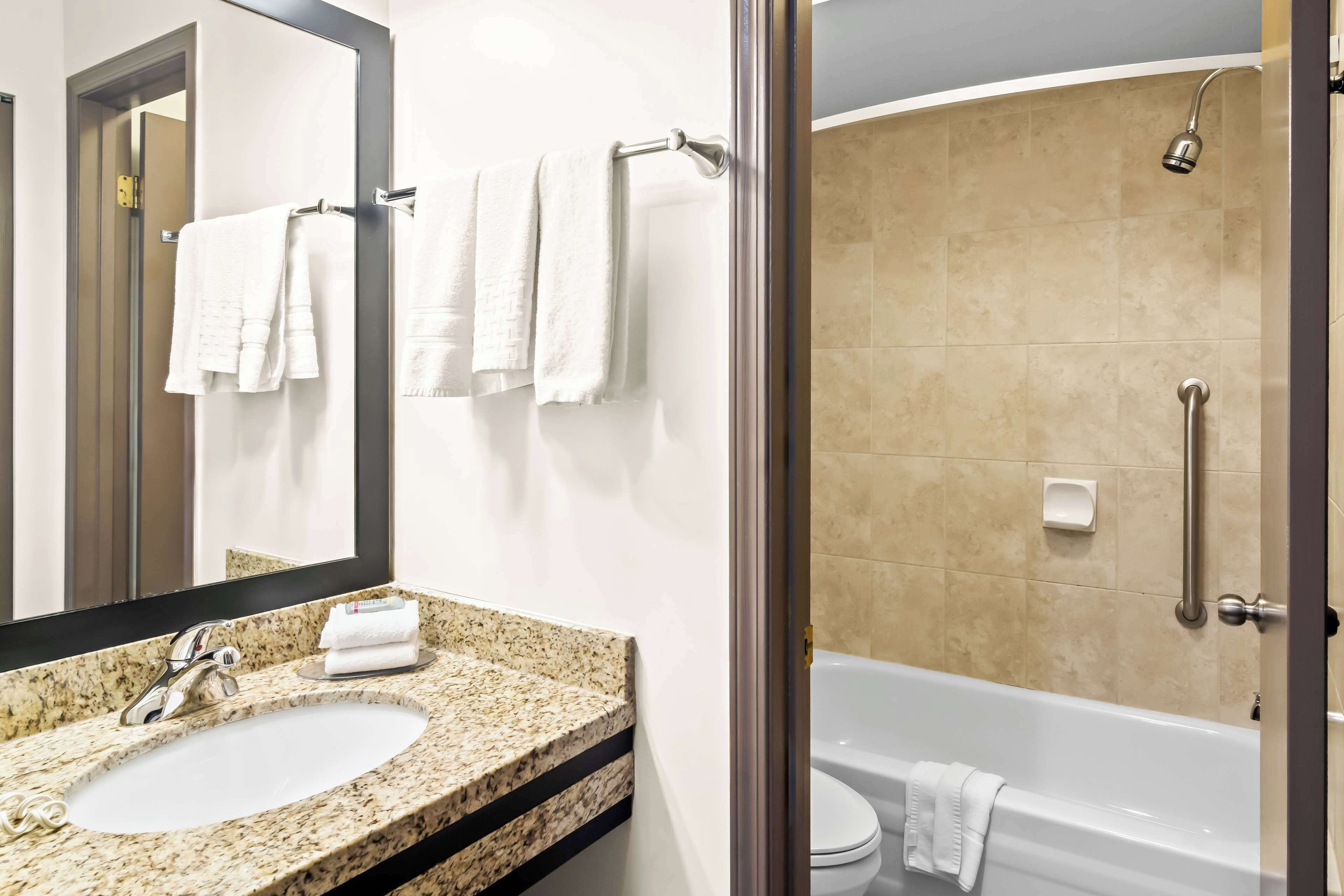 Un baño con lavamanos de encimera de granito, un espejo grande y una bañera blanca.