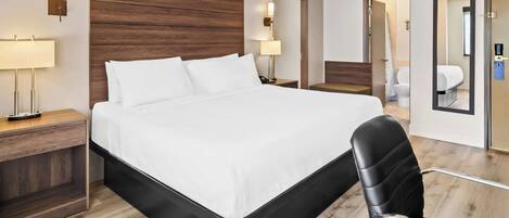 Une chambre d’hôtel moderne avec un grand lit, des tables de chevet, un fauteuil en cuir noir et une tête de lit en bois.