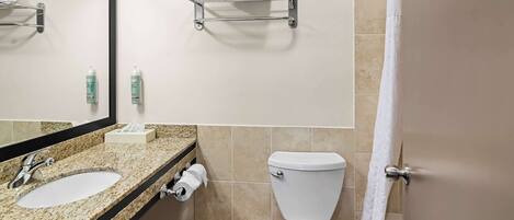 Un baño con lavamanos de encimera de granito, espejo, inodoro y toallero.