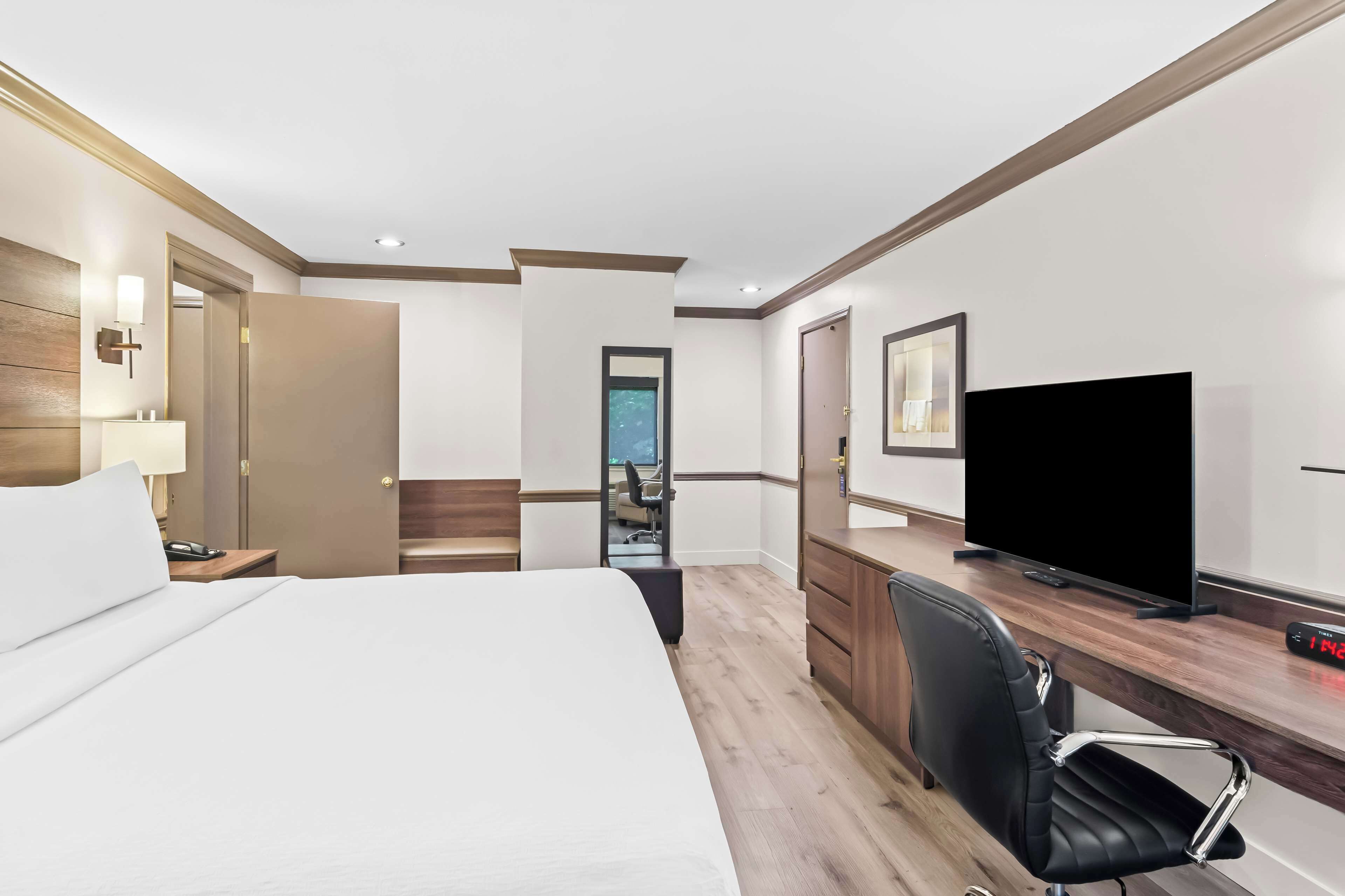 Habitación de hotel con una cama grande, un escritorio con televisor, una silla y una puerta que da a un baño.