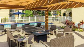 Une terrasse extérieure aménagée avec des meubles en osier, un foyer et une piscine en arrière-plan.