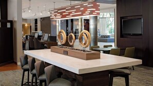 A modern bar area with a large island, bar stools, and a unique wooden centerpiece. - Courtyard by Marriott Fort Lauderdale North/Cypress Creek (Fort Lauderdale)