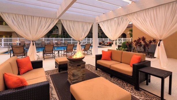 An outdoor seating area with a fire feature, pool in the background, and covered by white drapes. - Courtyard by Marriott Fort Lauderdale North/Cypress Creek (Fort Lauderdale)