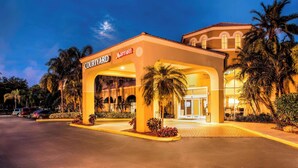 A Courtyard Marriott hotel entrance with a covered walkway, palm trees, and a parking lot. - Courtyard by Marriott Fort Lauderdale North/Cypress Creek (Fort Lauderdale)