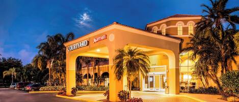 A Courtyard Marriott hotel entrance with a covered walkway, palm trees, and a parking lot.