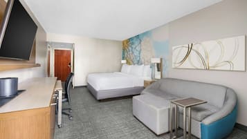 Une chambre d’hôtel avec un lit, un bureau avec un ordinateur, un canapé, une télévision et un tableau au mur.