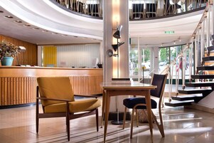 Un vestíbulo de hotel con una recepción, una zona de estar y una escalera.
