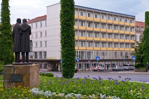 Un edificio con fachada moderna, una estatua de dos figuras y un paso de peatones.