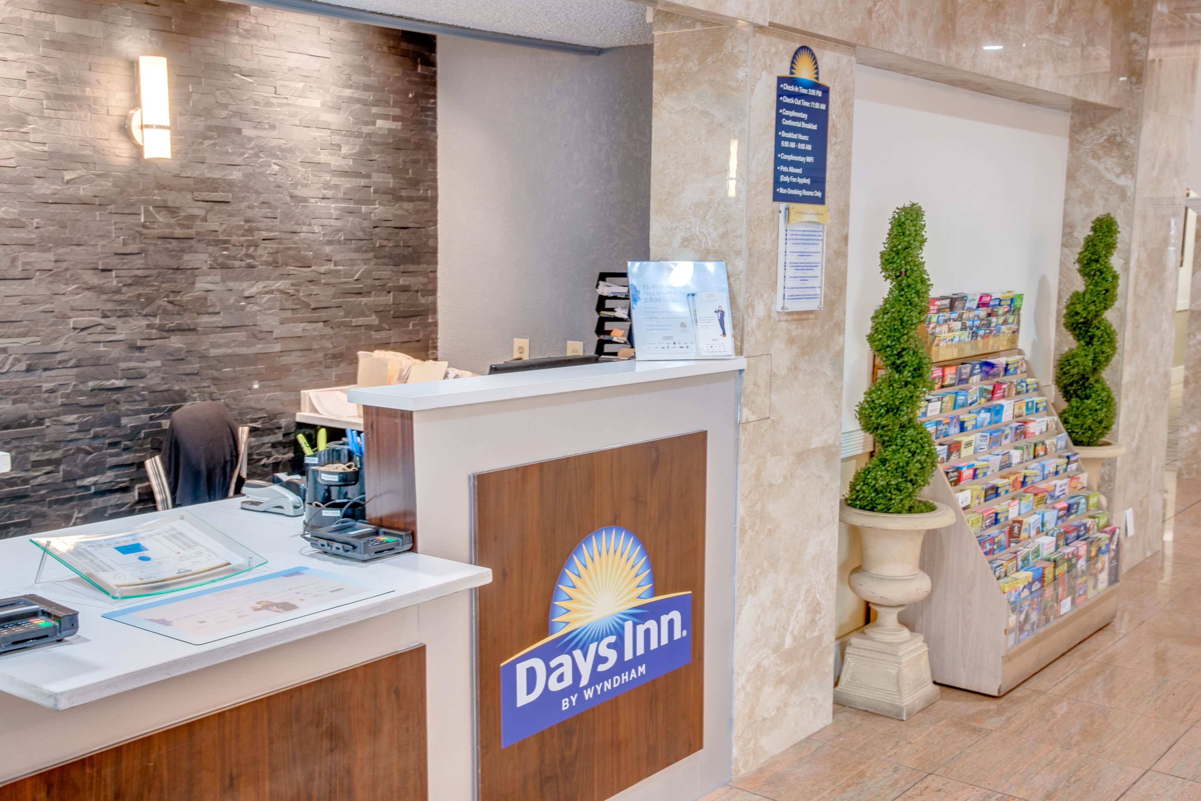 A reception desk with a Days Inn logo, a stone wall, and a bulletin board with brochures.