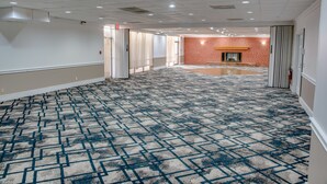 Un pasillo de hotel con alfombra estampada, paredes blancas y una pared de ladrillo con chimenea.