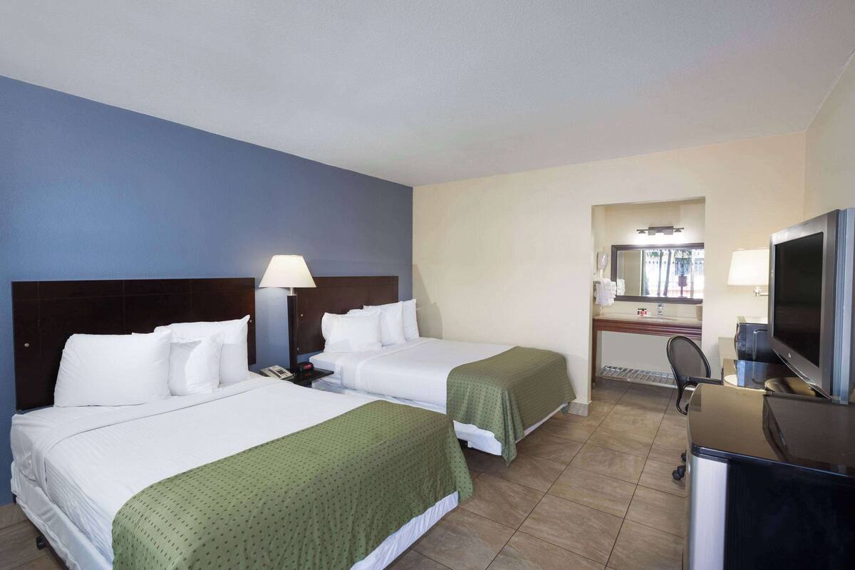 A hotel room with two beds, a desk, a TV, and a bathroom visible through an open door.