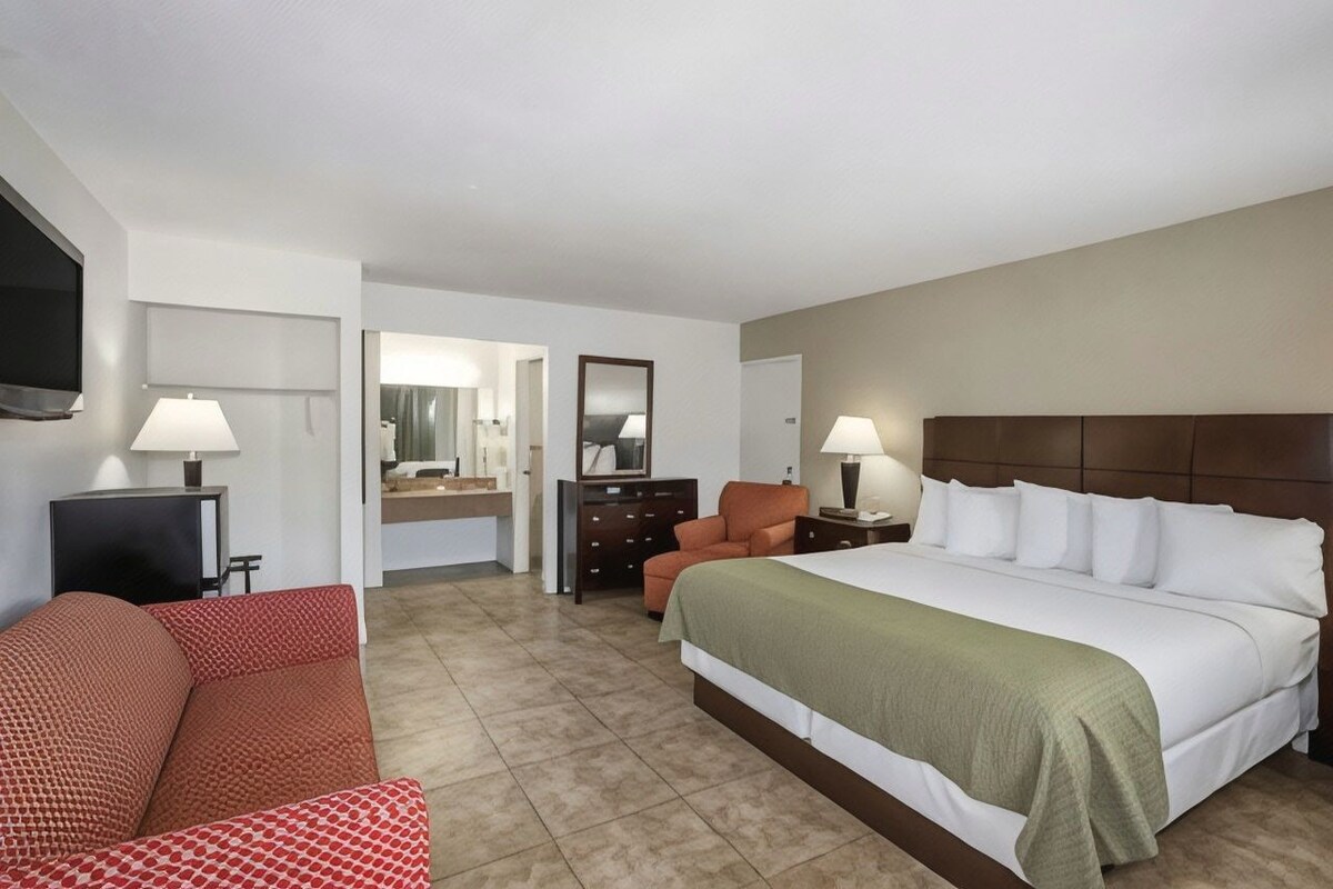 A hotel room with a bed, a sofa, a TV, a dresser, and a mirror.