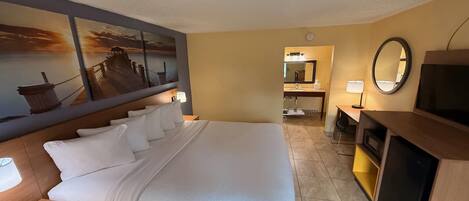 Une chambre d’hôtel avec un grand lit, un bureau, une télévision, un miroir et une salle de bain visible à travers une porte ouverte.