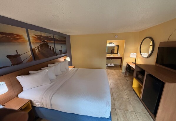 A hotel room with a large bed, a desk, a television, a mirror, and a bathroom visible through an open door.