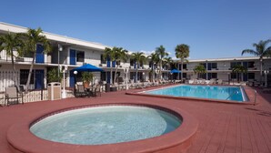 Un hotel con piscina, sillones de descanso y palmeras.