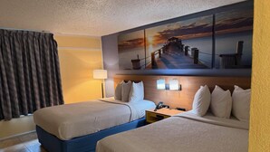 Habitación de hotel con dos camas, una mesita de noche, una lámpara y un cuadro de atardecer en la pared.