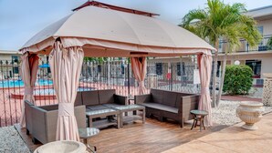 Un espacio de estar al aire libre cubierto con mobiliario de mimbre, una mesa de vidrio y una urna decorativa.