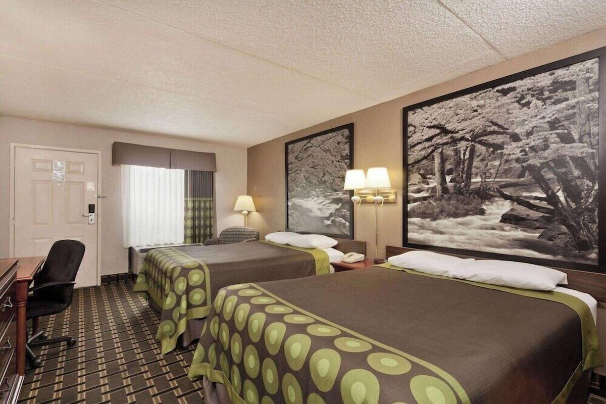 A hotel room with two beds, a desk, a chair, and a large window with curtains.