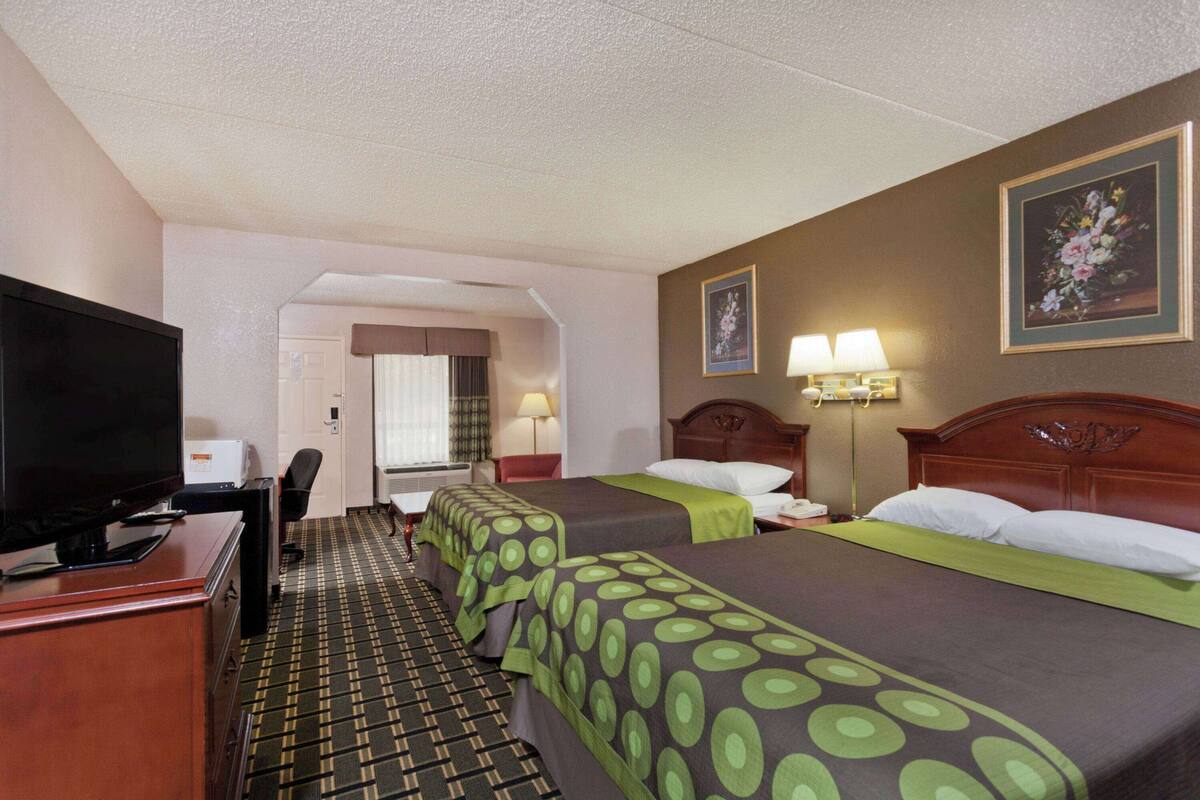 A hotel room with two beds, a television, a desk, and a chair.
