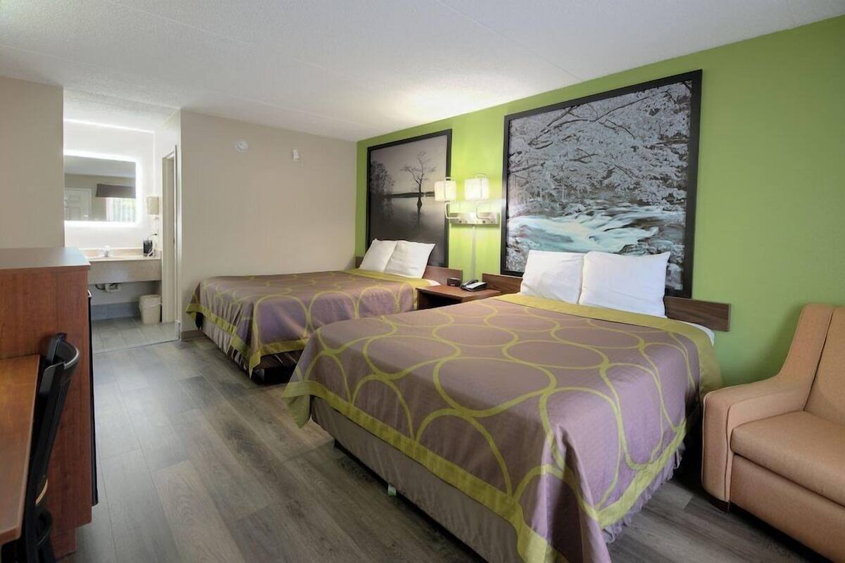 A hotel room with two beds, a desk, a chair, and a bathroom visible in the background.