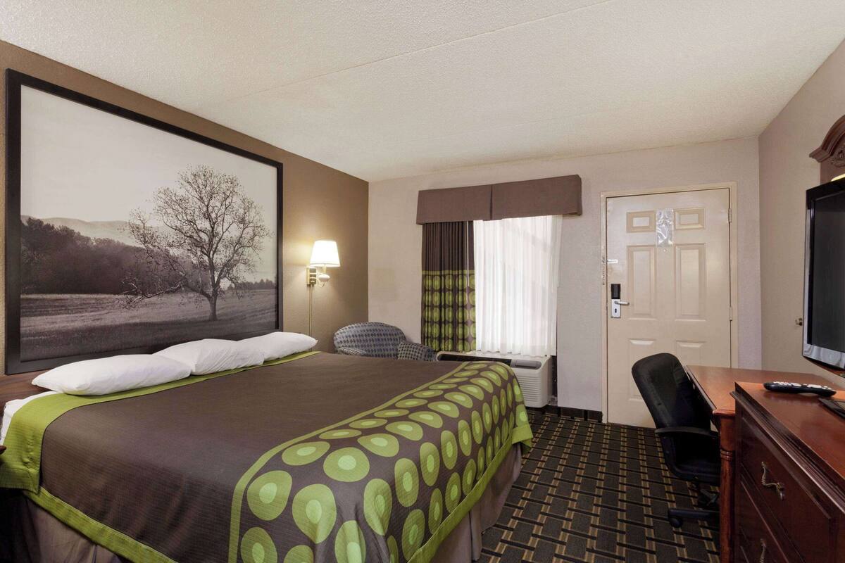 A hotel room with a large bed, a desk with a computer, a television, and a window with curtains.