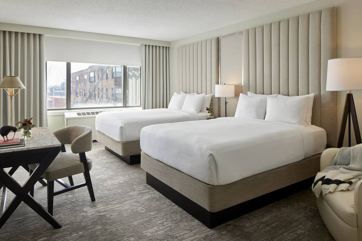 A hotel room with two beds, a desk, and a chair.