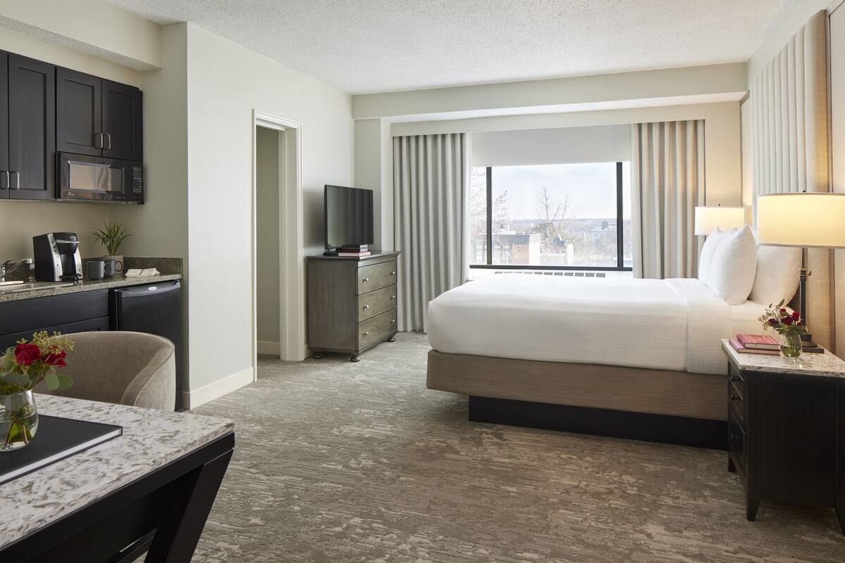 A hotel room with a bed, a desk, a chair, a TV, a lamp, and a window with curtains.