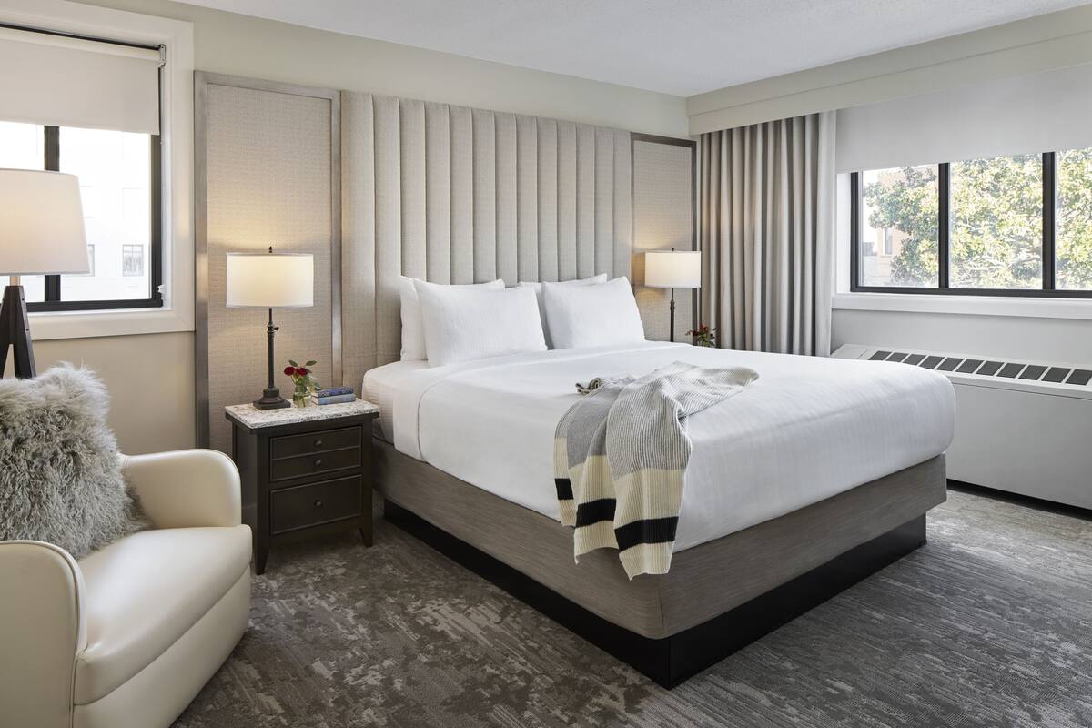 A modern hotel room with a large bed, bedside lamps, a small desk, and a chair.