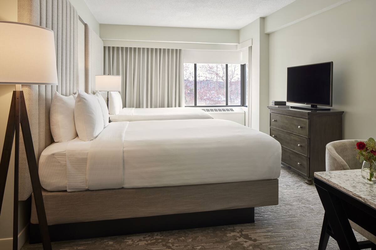 A hotel room with a large bed, a TV, a desk, and a window with a view of trees.