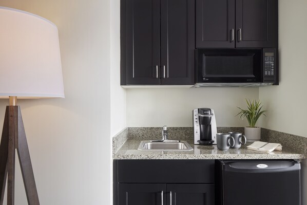 Una cocina con armarios oscuros, un microondas, una cafetera y un lavabo.
